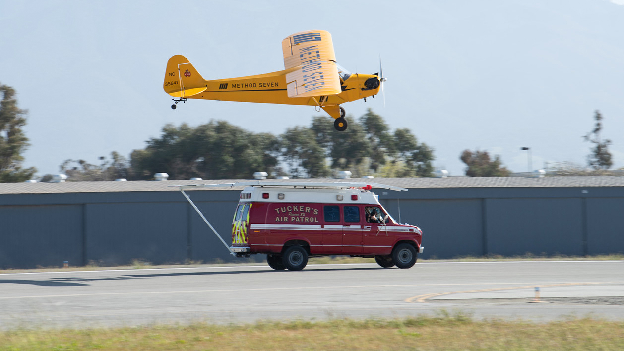 Justin Ramsier drives a 1990 ambulance while Eric Tucker practices landing his J-3 Cub on a platform attached to the ambulance roof.